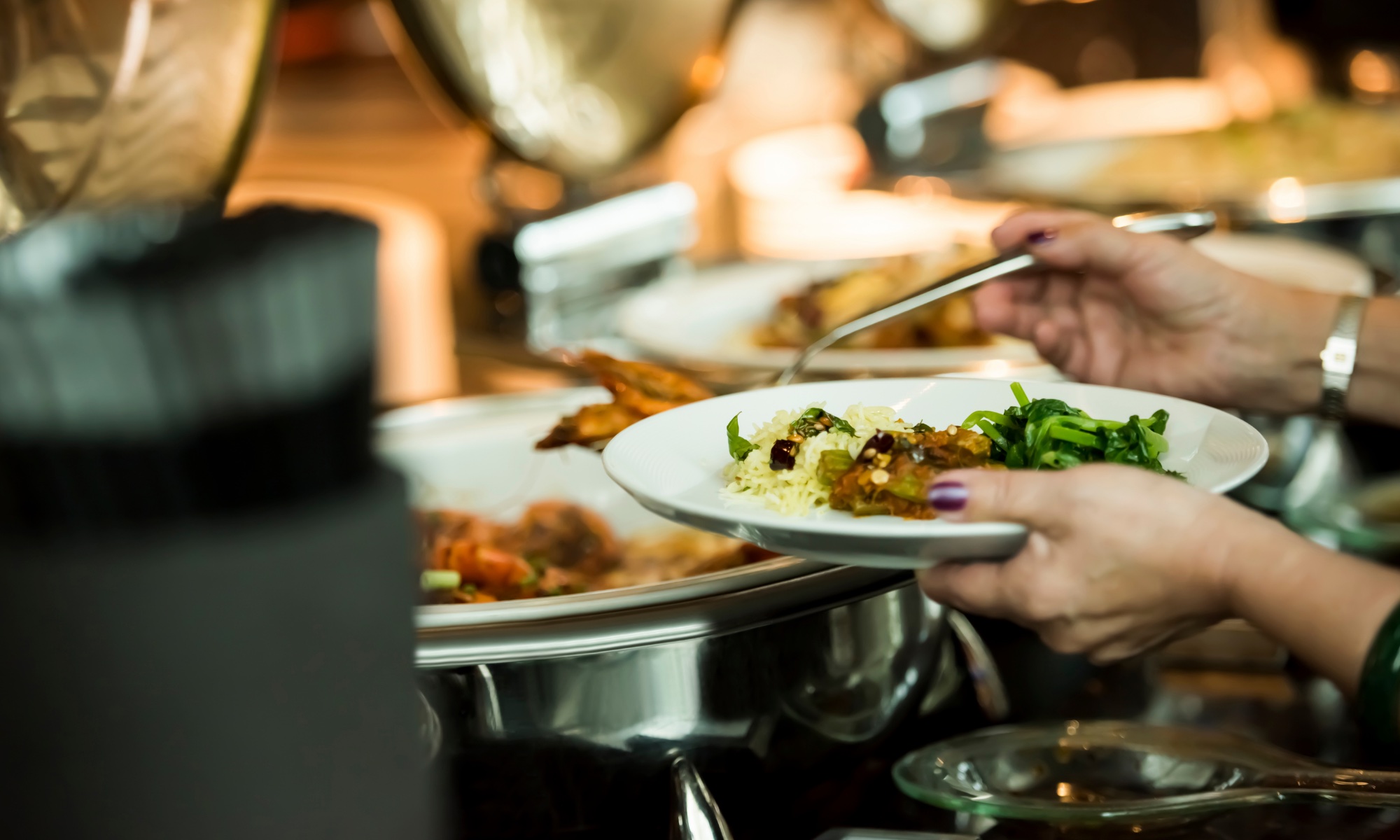 Guest filling a plate at a catered holiday party buffet with chafing dishes
